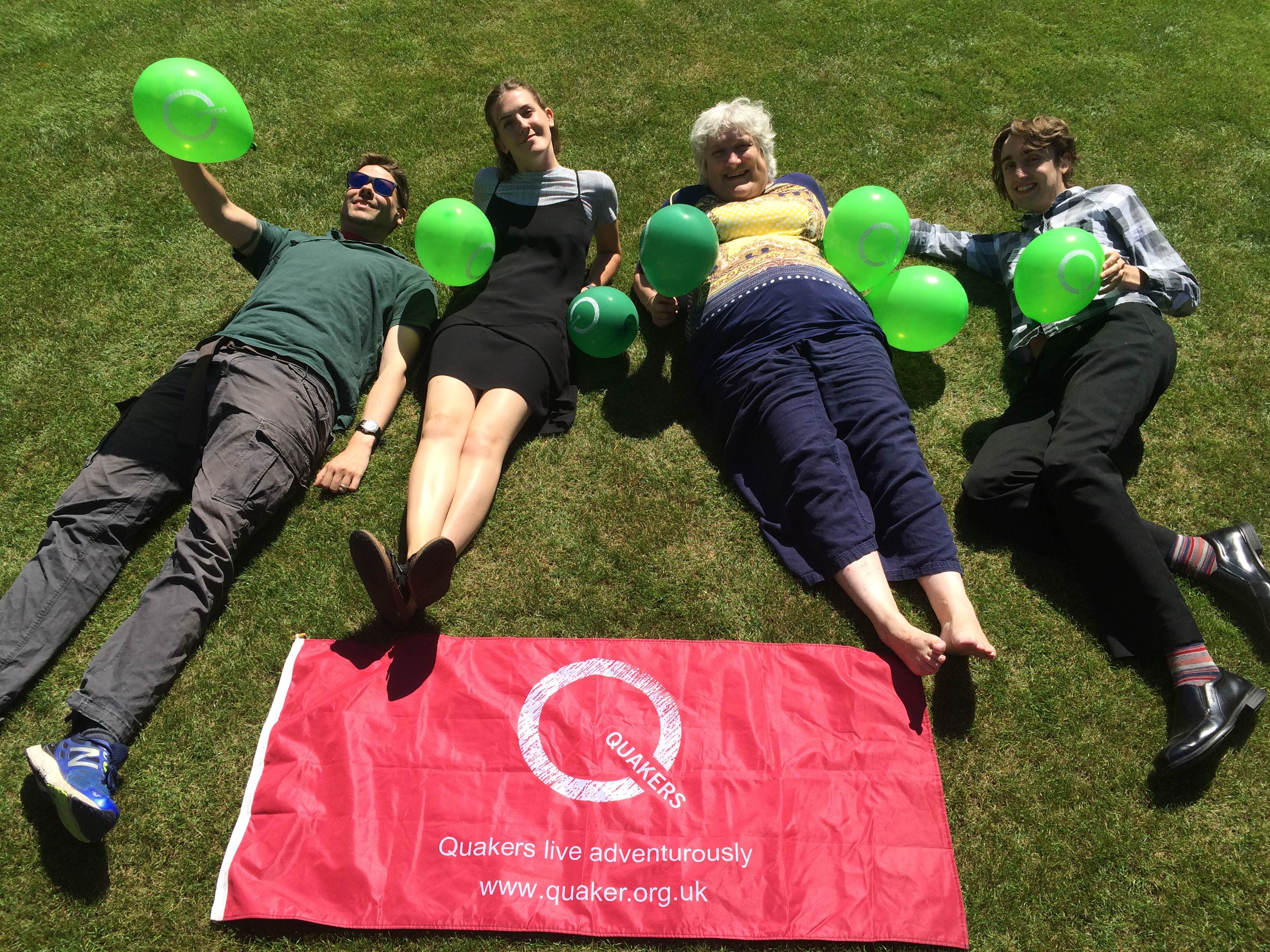 4 people laying on grass holding Quaker balloons