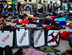 people lying on the ground pretending to be dead. Sign reads stop airport expansion stay grounded. 