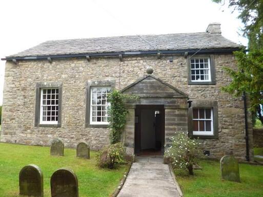 One storey stone cottage with flowers around the door is located within a Quaker burial ground. 