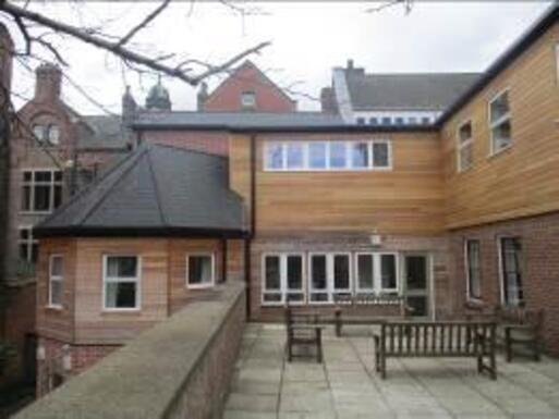 Extended building with courtyard and balcony with modern wood panelling covering old brickwork. 