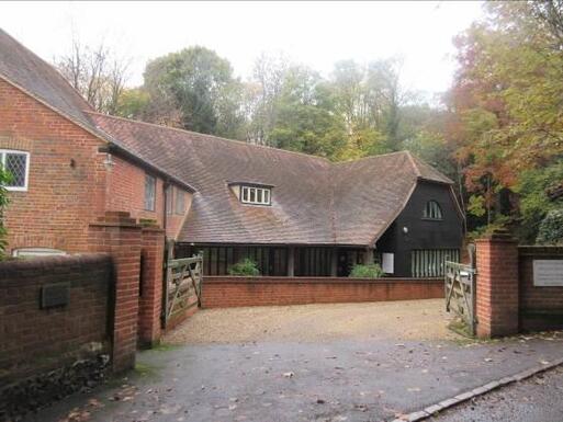 Brick dwelling with long sweeping roof and gated driveway to front.