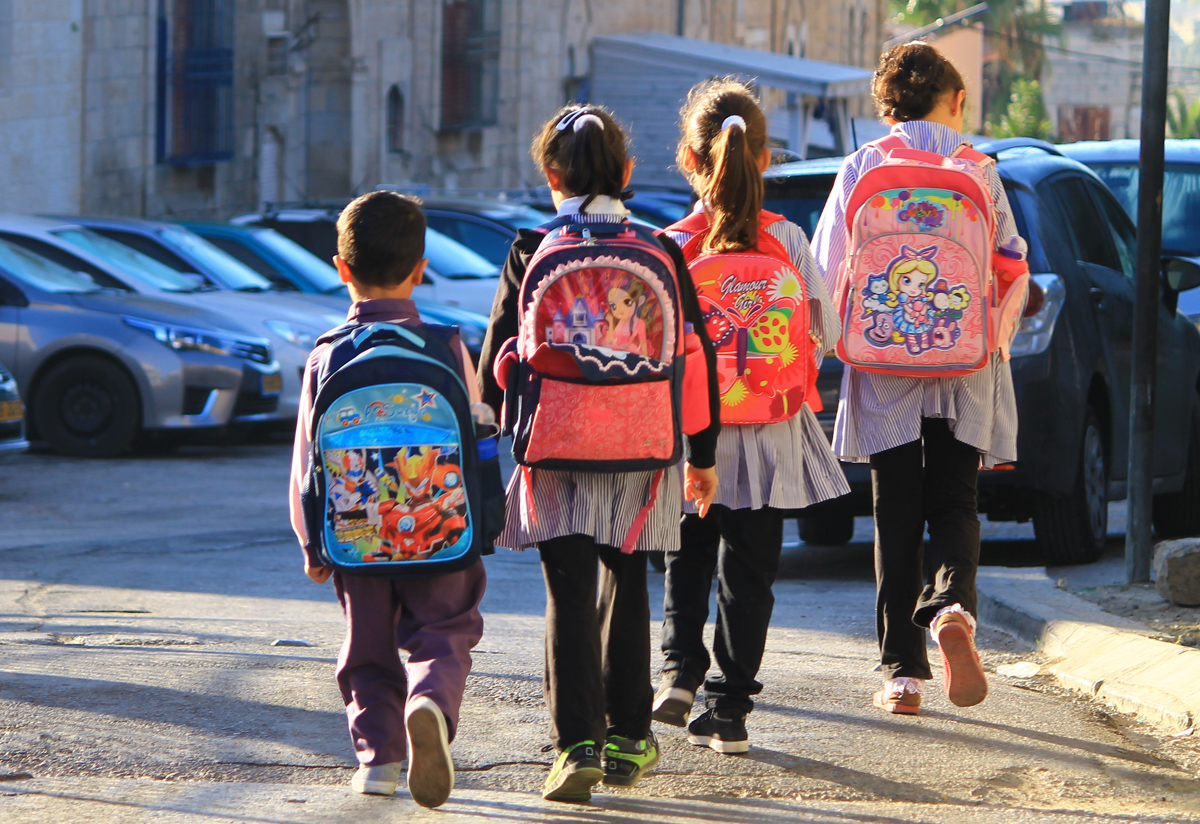 Four children wearing school uniform and carrying backpacks walking to school