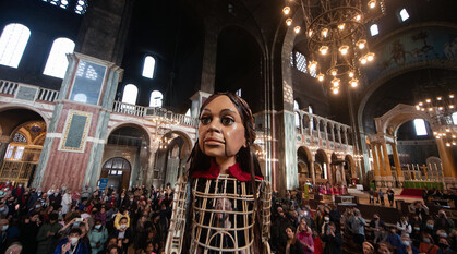 A large puppet inside Westminster Cathedral with a crowd on lookers surrounding her