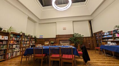 A table laid for dinner in a book lined room with a high glass ceiling and a circular light 