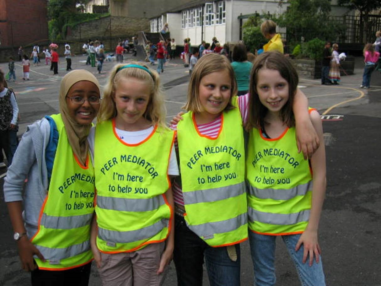 four girls in playground wearing florescent tabards saying Peer mediator I'm here to help you