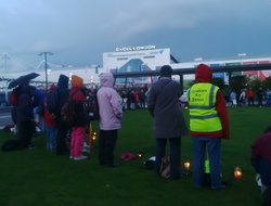 A circle of people of many faiths and none stand in a circle by candlelight outside the DSEI Arms Fair at London's Excel Centre.