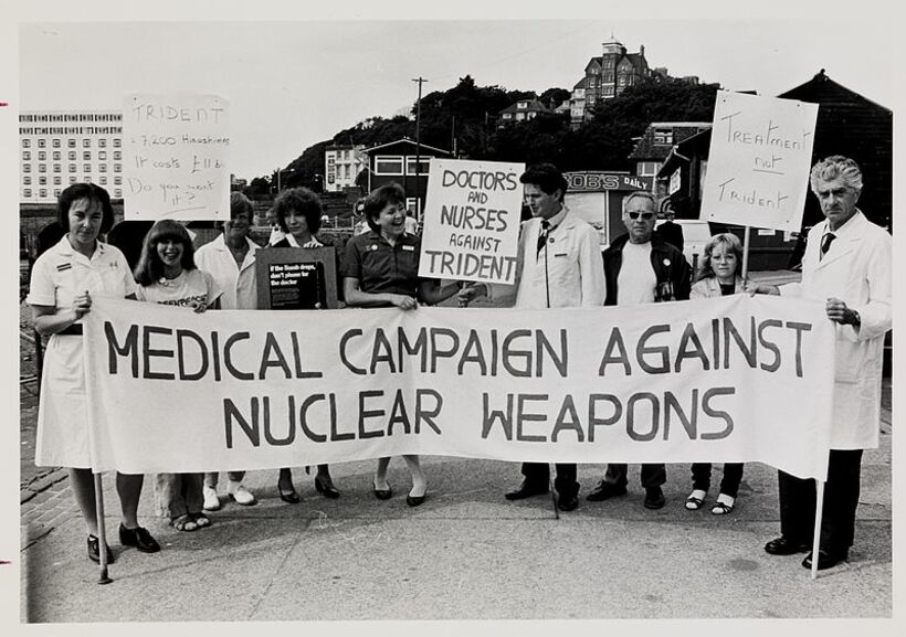 A group of doctors and nurses hold up a "Medical Campaign Against Nuclear Weapons" banner and placards