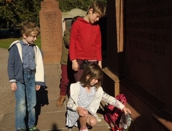 Four children lay a wreath of red and white poppies a tthe foot of the Cavell memorial