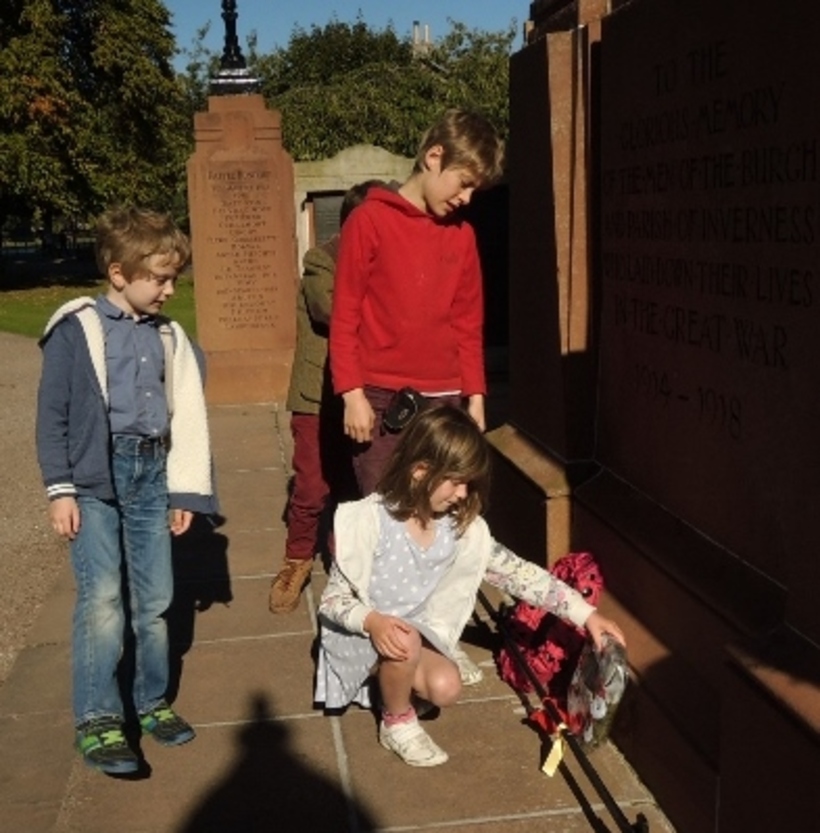 Four children lay a wreath of red and white poppies a tthe foot of the Cavell memorial