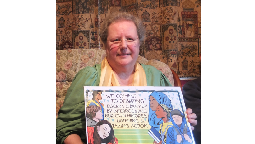 Maria Haines holding a poster from AFSC with the words 'we commit to resisting racism and bigotry by interrogating our own histories, listening and taking action'