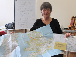 A woman holding up a map of the UK and Ireland and a pack entitled 'Welcome to Lancaster'