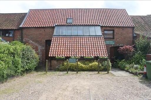 Red brick building with low roof and green sign reading 'Quaker Meeting House'.