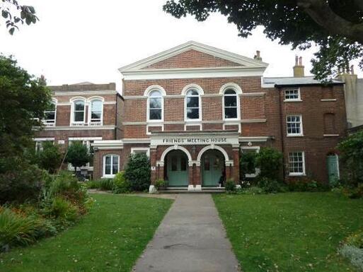 Large brick house with double arches flanking four entrance doors, lettering reading 'Friends Meeting House' is over the porch. 