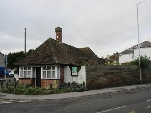 Small white bungalow with double bay windows at front and small sign above central front door. 