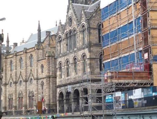 Large gothic stone building with long arched windows and arched walkway to entrance. 