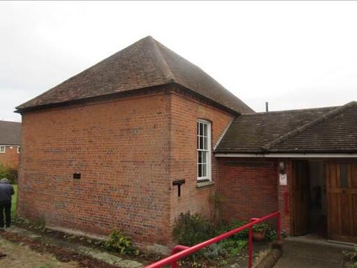 Small brick bungalow with slope leading to entrance doors. 