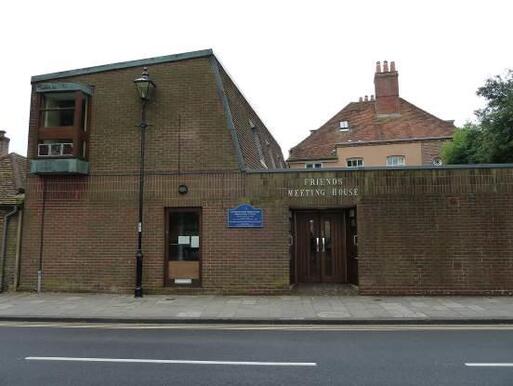 Distinct asymmetrical brick building with small second-floor window and large 'Friends Meeting House' lettering above entrance doors. 