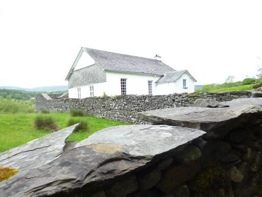 White cottage with long period windows surrounded by stone wall, set within isolated field landscape. 