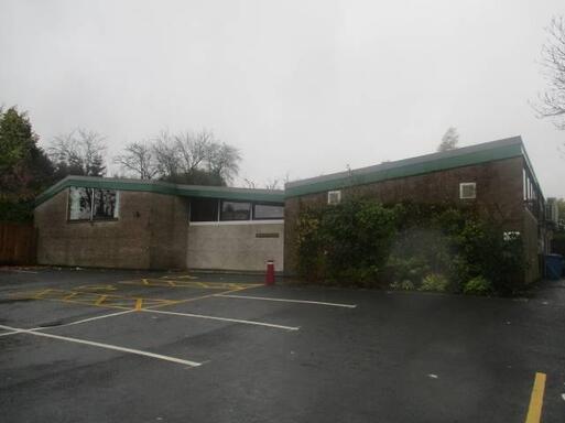 Large wide brick building with asymmetric windows and diagonal flat roof, set within a large car park.