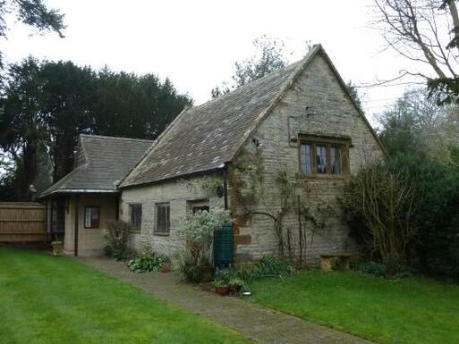 Old grey stone cottage with creeping plants set within a large garden.