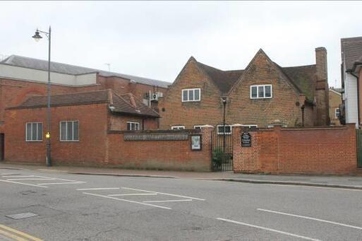 Large brick house with gable roof, separated from the main road by a high red brick wall.