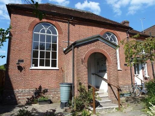 Small brick chapel with large arched windows and decorative entrance porch.