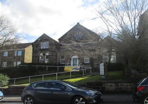 Large grey stone building with long winding ramp to front door, in steep gardens.