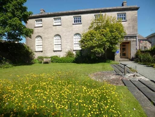 Large grey stone building with wide gardens and arched windows.