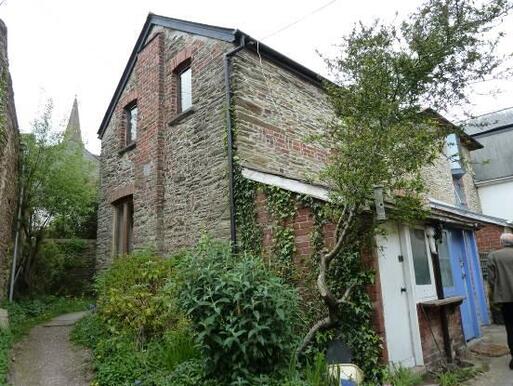 Old brick house with small entrance porch set along a small winding path.