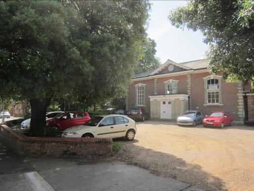 Large brick building with stone detailing surrounding its long windows and entrance porch.