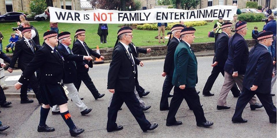 Veterans parading past a banner which says 'War is not family entertainment'