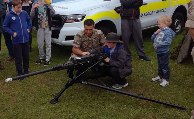 A child is shown a machine gun by soldiers. 