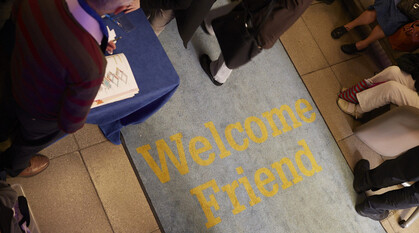 People walking over a mat with the words 'Welcome Friend' written on the mat