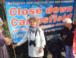 A group of protestors stand in front of a large blue banner which reads 'Close down Campsfield'