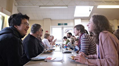 Two rows of people at tables laugh and eat