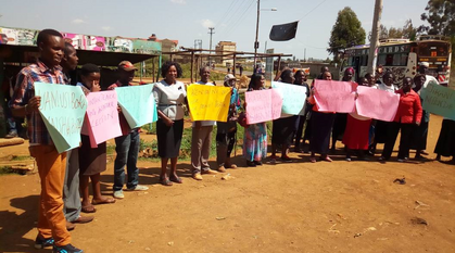 A group of people standing outside in the sunshine holding placards calling for nonviolence during elections in Kenya