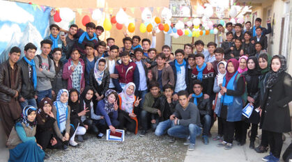 A group of Afghan peace volunteers in a courtyard with balloons. Several are making the peace sign 'v' with their fingers