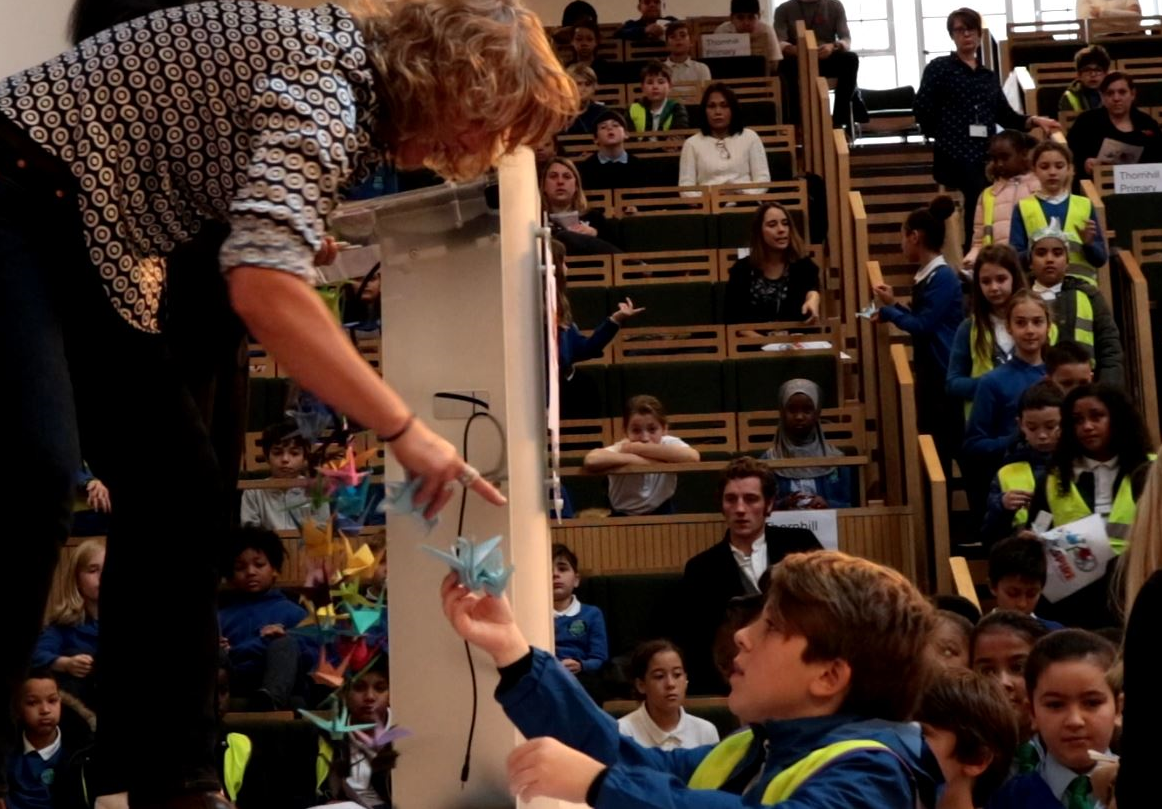 child offers paper crane for peace tree