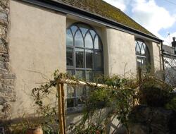 a single storey stone building with large windows is photographed from a neighbouring garden. 