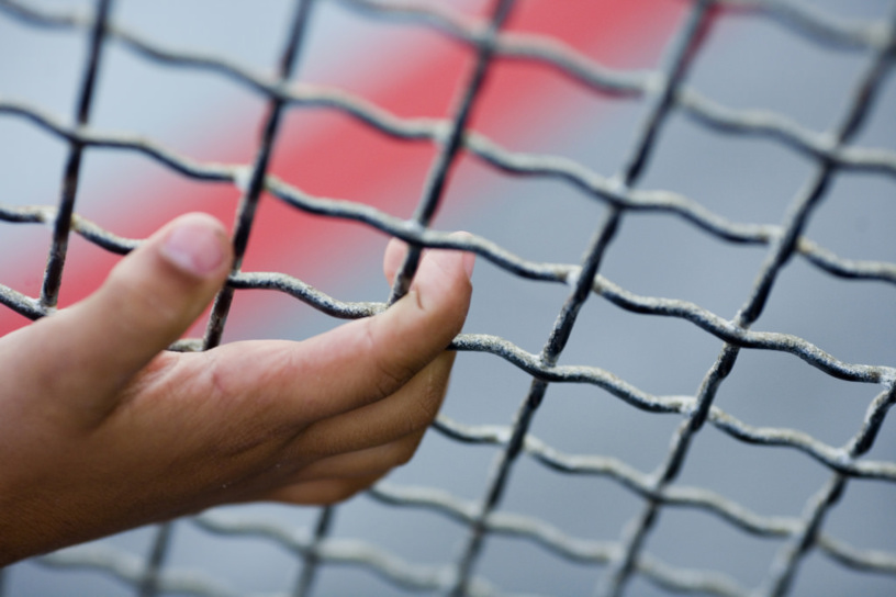 child's hand clings to wire fence