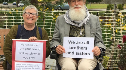 woman sat on a bench smiling and man with long beard and a hat in a wheelchair 