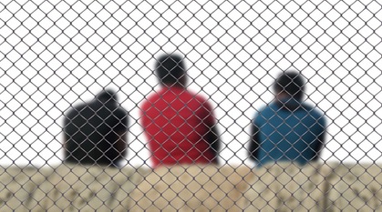 three men sat on concrete behind a chain link fence 