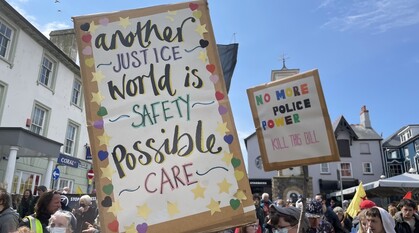 Protestors with placards at an anti-policing bill protest. Focused placard says 'another world is possible: justice, safety, care'