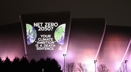 Text projected on a building at night reads "net zero 2050? your climate 'ambition' is a death sentence"