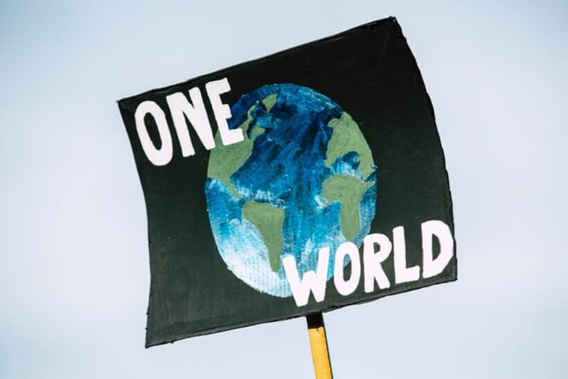 A handmade poster/placard with a painting of the Earth and the words 'One World' written on it