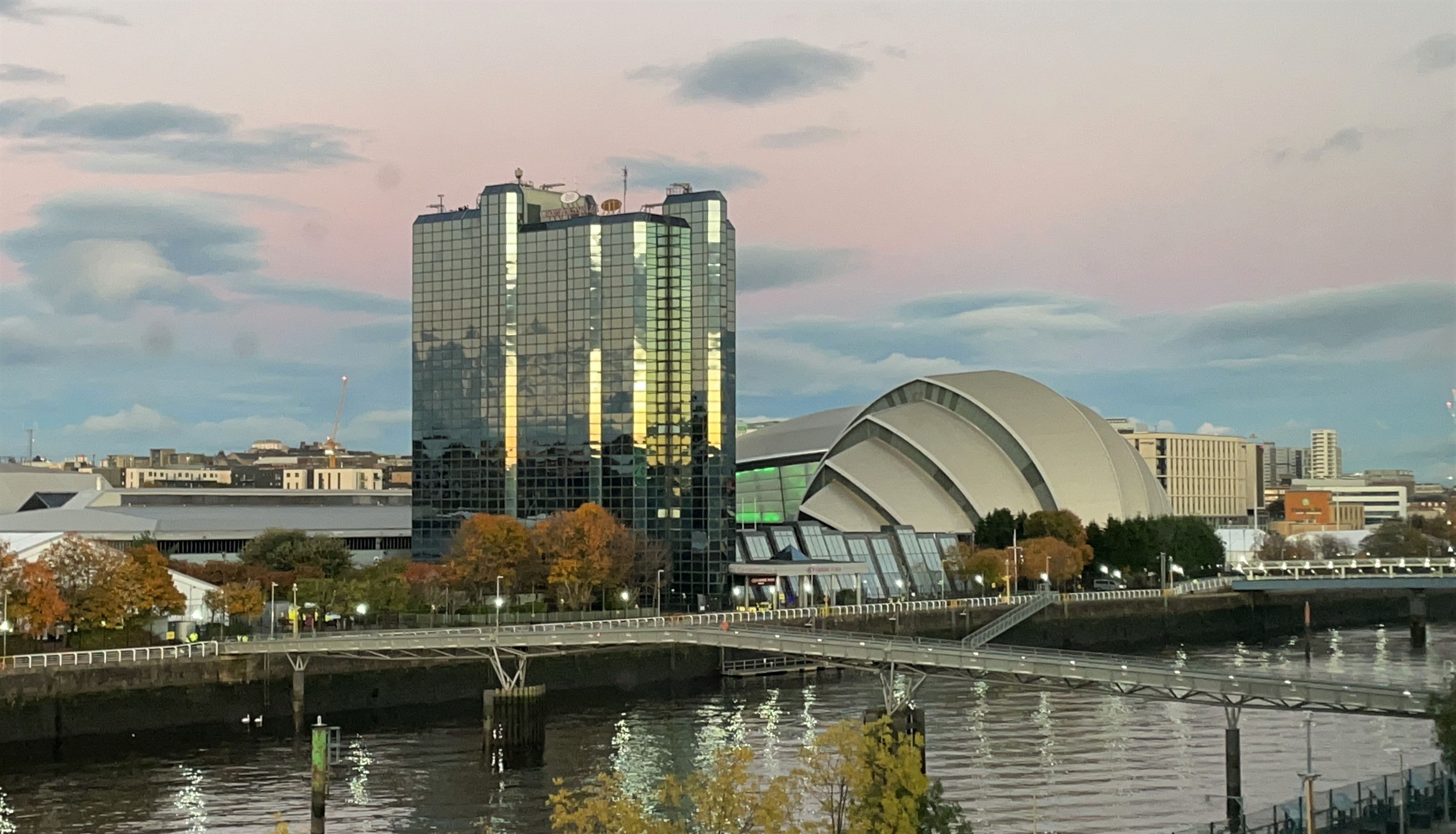 A tall shining building and an armadillo-shaped building beside a river 