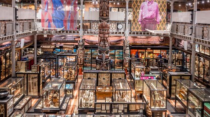 The inside of Pitt Rivers museum showing a floor covered in old, glass display cases. At the back of the room a totem pol stands high.