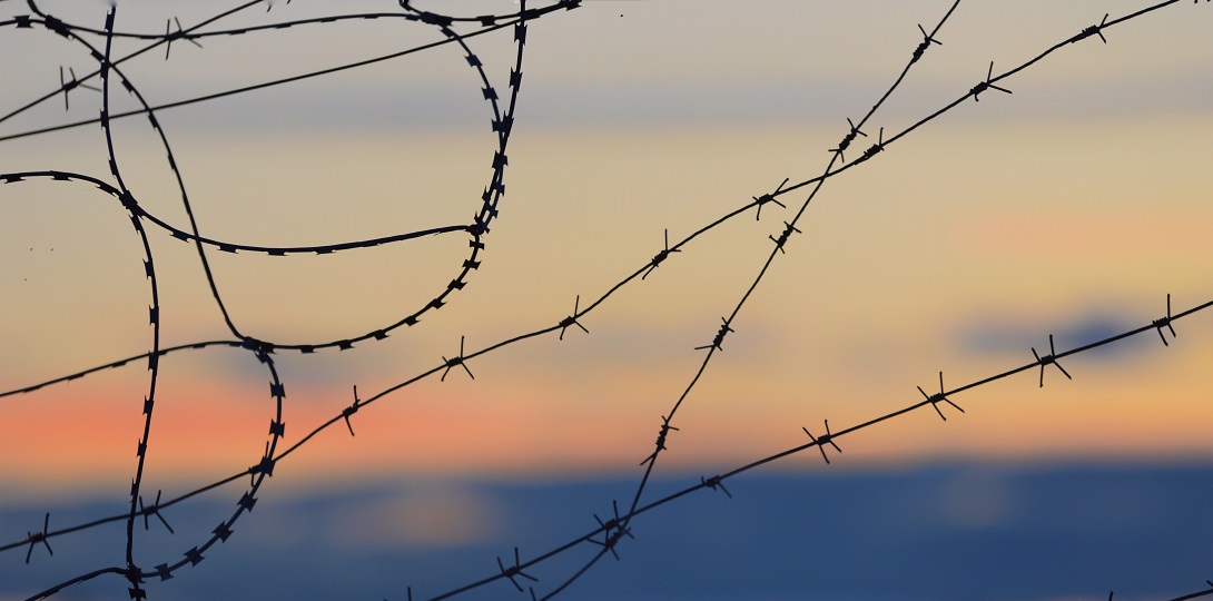 A barbed wire fence with an orange sky beyond