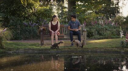 Still from His Dark Materials: Lyra and Will sat on a bench in Oxford with their daemons, but in two different worlds