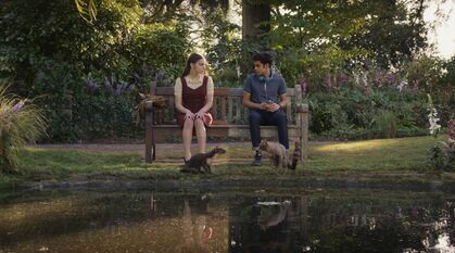 Still from His Dark Materials: Lyra and Will sat on a bench in Oxford with their daemons, but in two different worlds